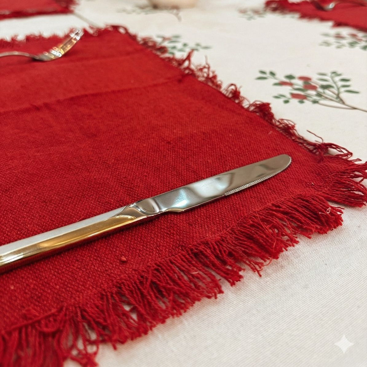 Red placemat with fringe on a table setting with silverware and a floral centerpiece.