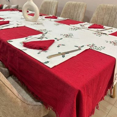 Dining table set with red tablecloth, placemats, and cutlery on a floral-patterned tablecloth.