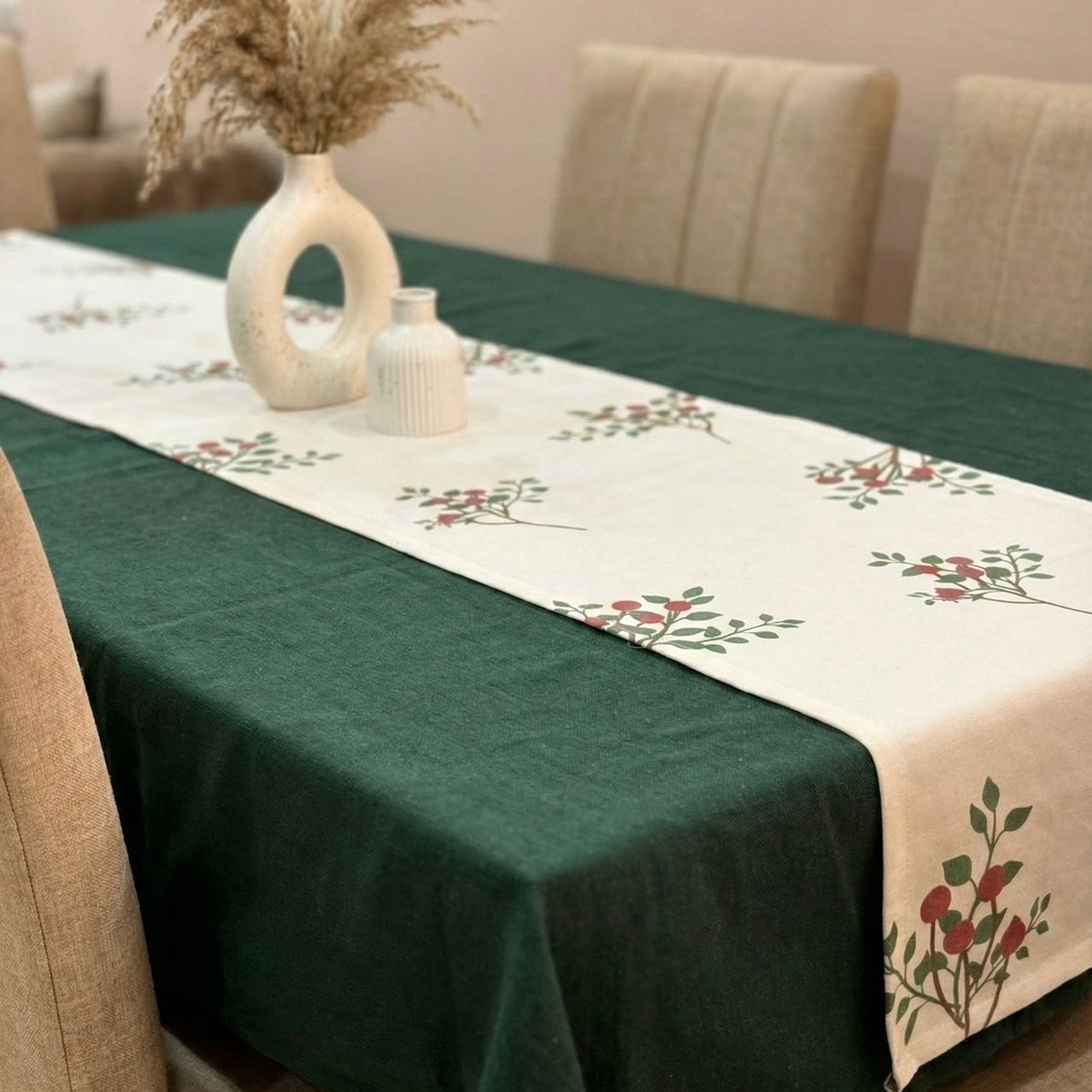 Dining table with green tablecloth and floral runner, decorated with vases and plants.
