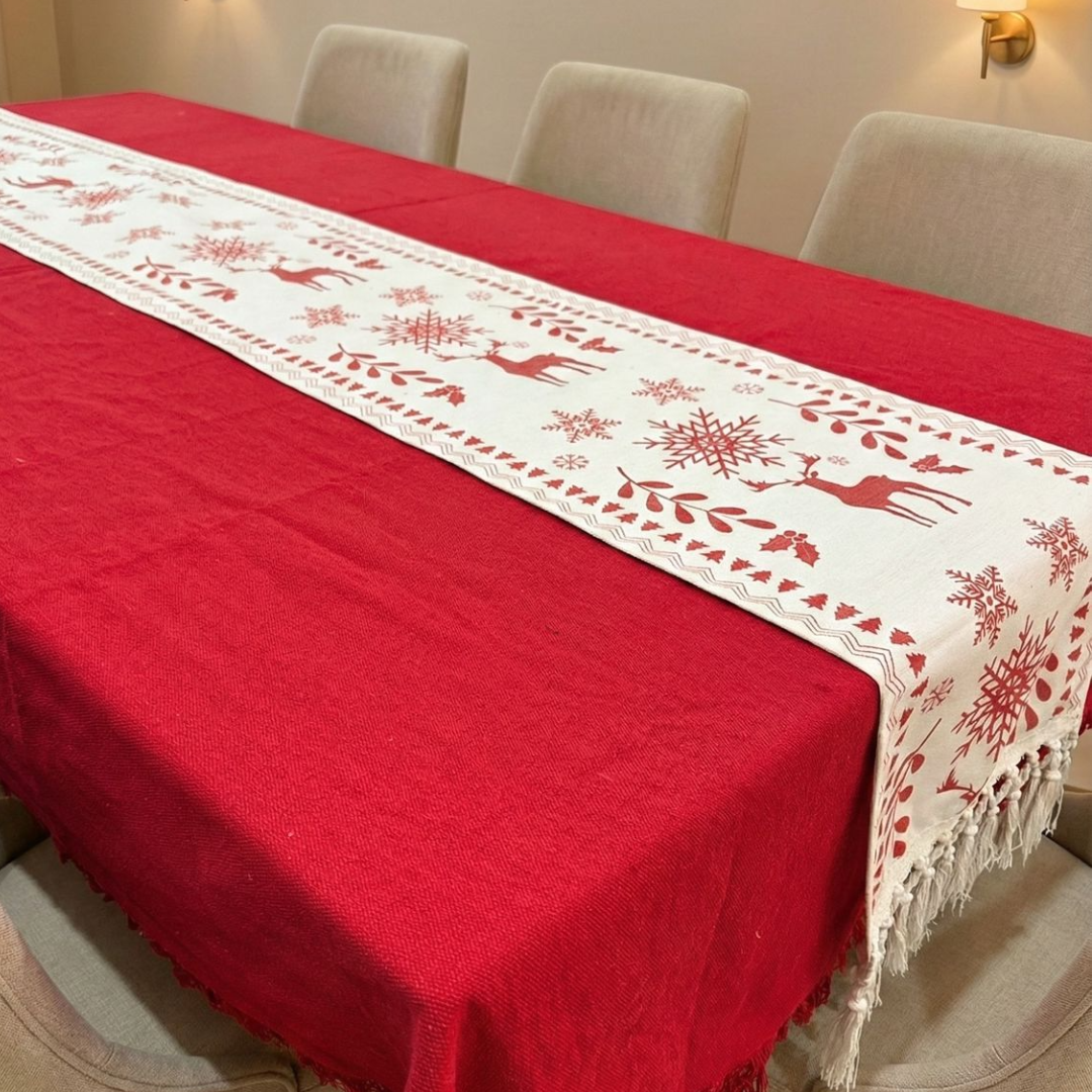 Red tablecloth with a white embroidered runner featuring reindeer and snowflakes on a dining table.