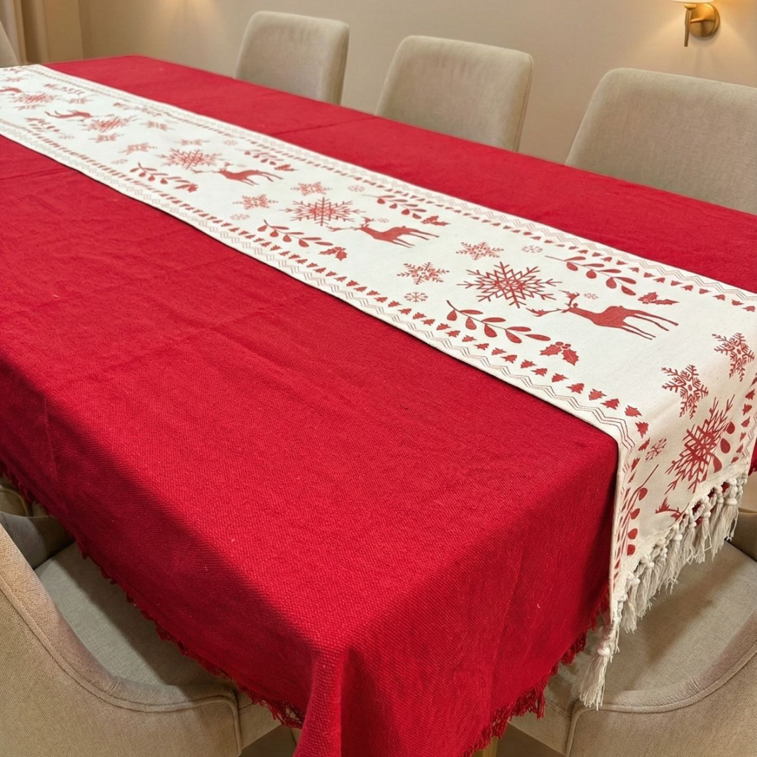 Red tablecloth with a white embroidered runner featuring reindeer and snowflakes on a dining table.