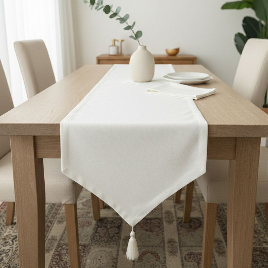 Dining table with a white tablecloth and tassels in a bright room.
