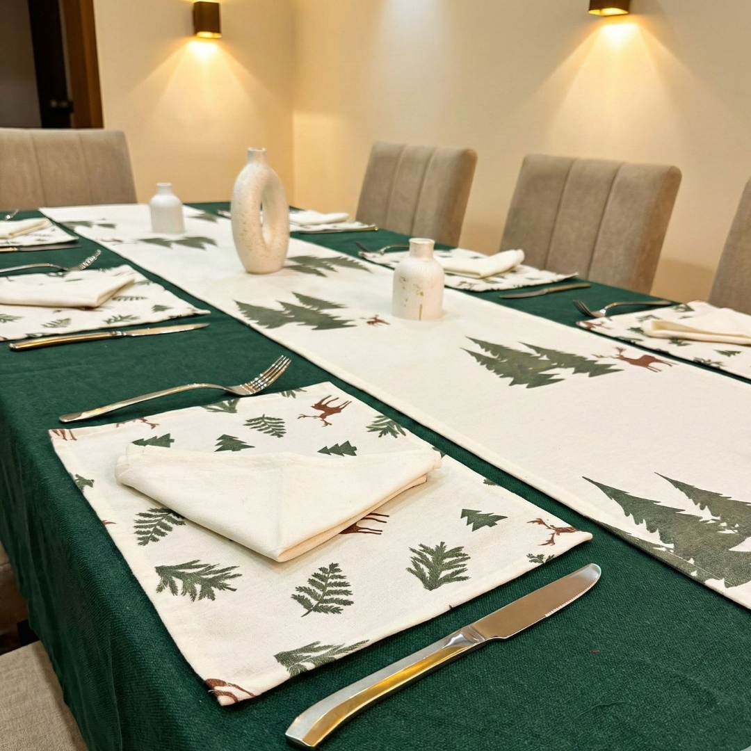 Dining table set with green placemats and napkins featuring tree patterns, surrounded by chairs.